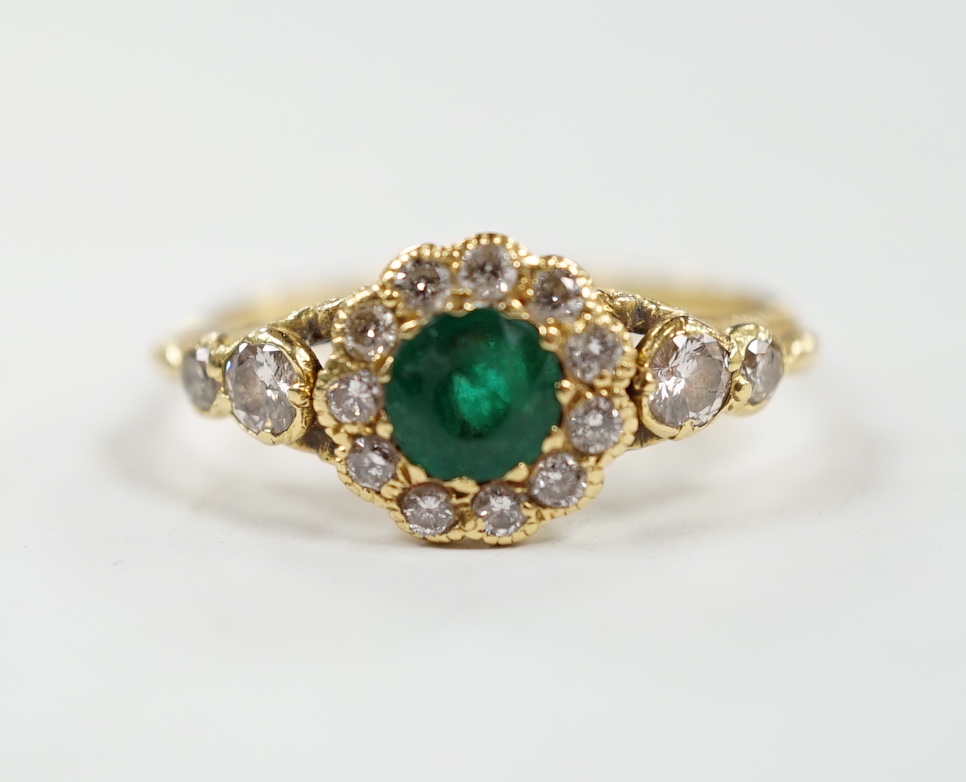 A Victorian style yellow metal emerald and diamond set circular cluster ring, with graduated diamond set shoulders, size N, gross weight 3.7 grams.